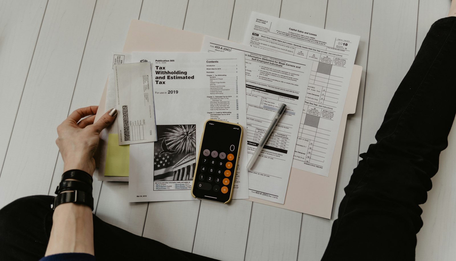 A desk covered with printed account and compliance forms, a calculator, a pen and a smartphone resting on the paperwork